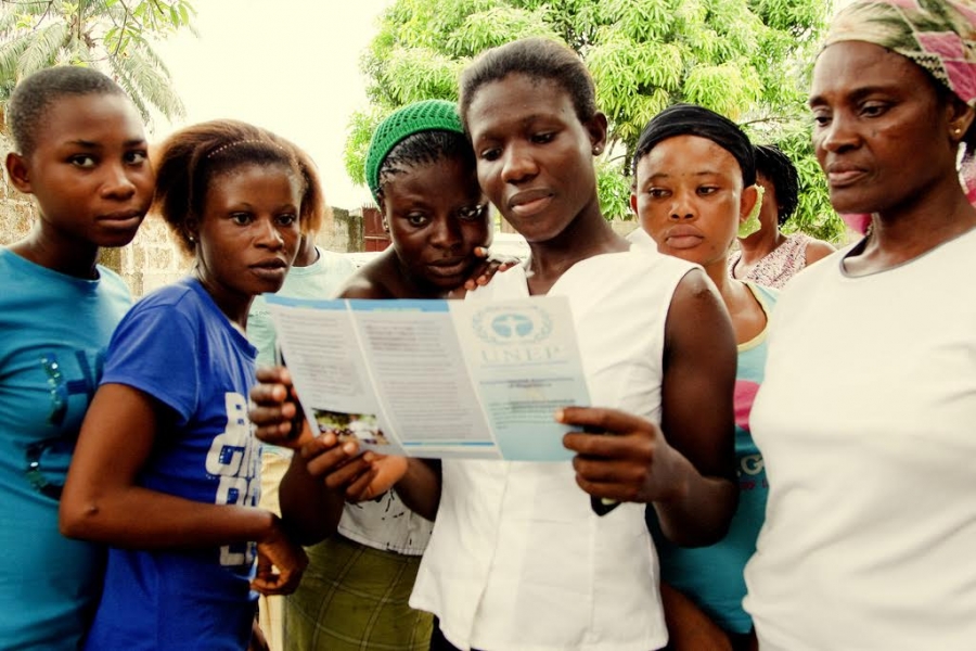 Six African young women standing while reading a UNEP leaflet on the hands of one of them